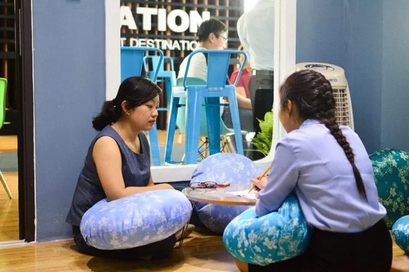 Hai phụ nữ ngồi đất với gối tựa màu xanh, trò chuyện tại trung tâm giáo dục Edusa, trong không gian học tập hiện đại