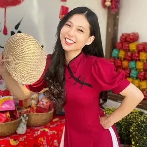 Hình ảnh Thu Hằng trẻ trung với nụ cười rạng rỡ, mặc áo dài đỏ, tay cầm quạt tre, nền là các gói quà nhiều màu sắc trang trí.